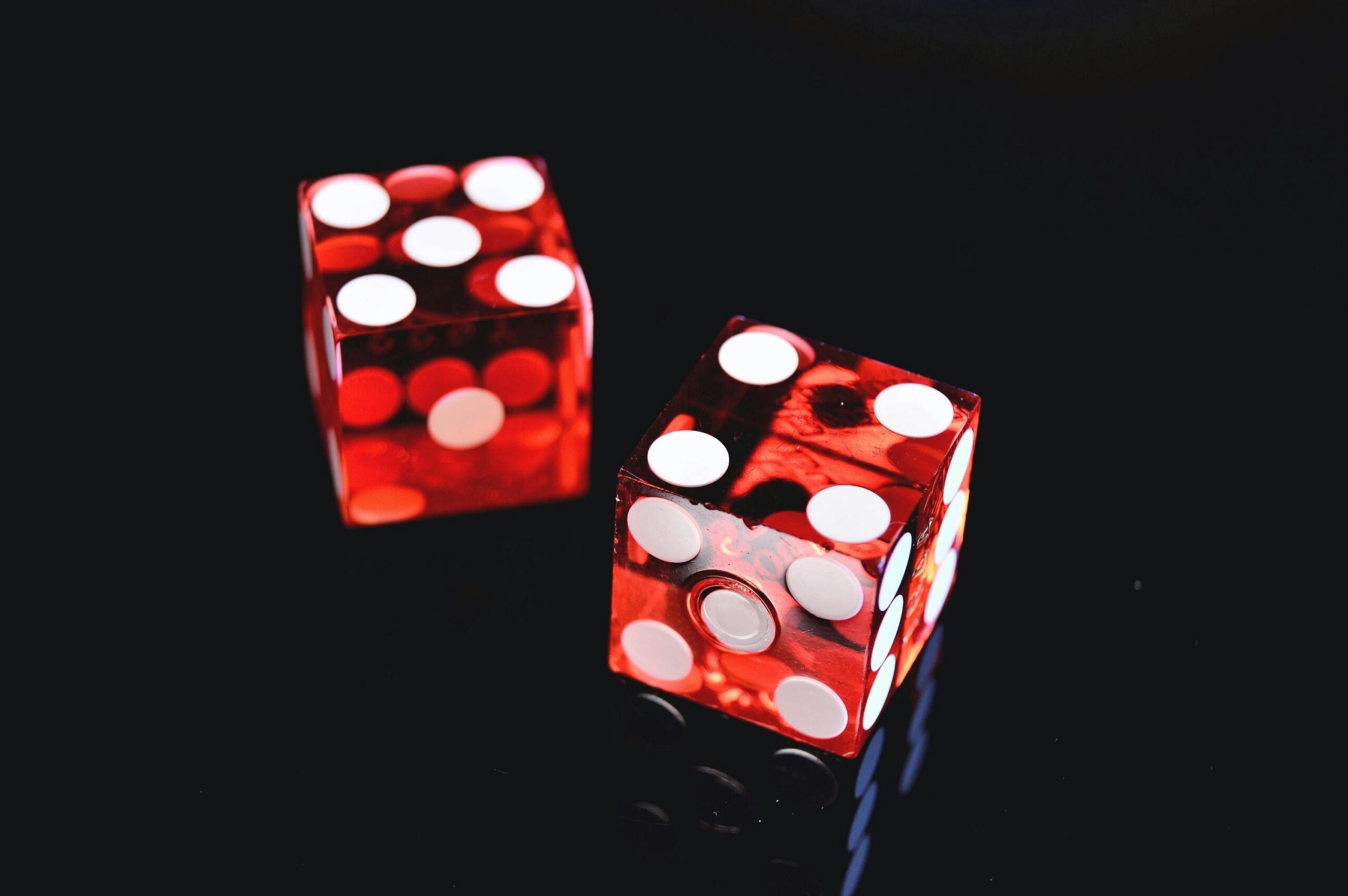 Close-up of two red dice on a shiny black background symbolizing luck and chance.